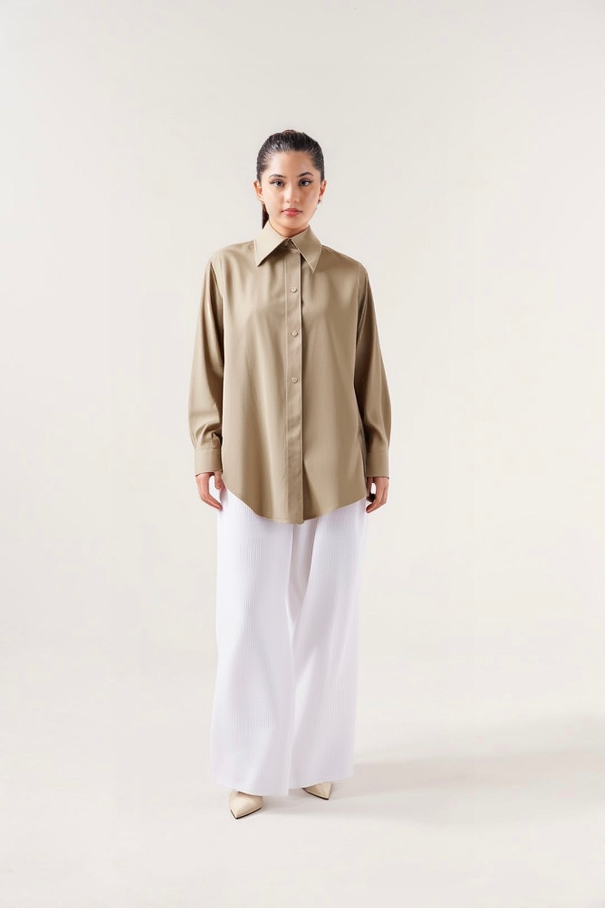 Person wearing a beige shirt and white pants on a plain background